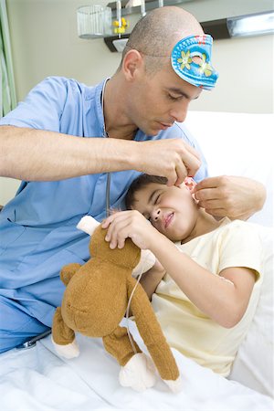 Boy lying in hospital bed, holding stuffed animal while doctor puts drops into boy's ear Stock Photo - Premium Royalty-Free, Code: 696-03393972