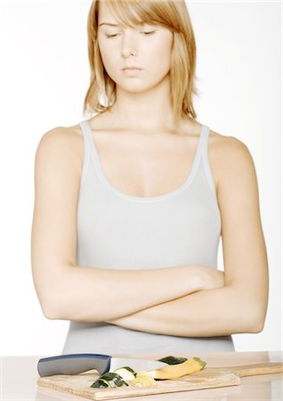 sad body language - Young woman with arms folded looking down at sliced zucchini Stock Photo - Premium Royalty-Free, Code: 696-03400134