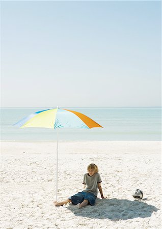 Boy sitting on beach under parasol Stock Photo - Premium Royalty-Free, Code: 696-03400417