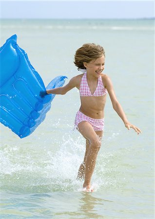 Girl running in surf at beach, carrying raft Stock Photo - Premium Royalty-Free, Code: 696-03400798