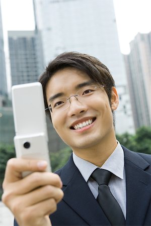 simsearch:696-03401126,k - Homme d'affaires brandissant un téléphone cellulaire, souriant Photographie de stock - Premium Libres de Droits, Code: 696-03401128