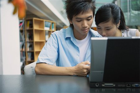 simsearch:632-01271145,k - Jeune couple à l'aide d'ordinateur portable dans la bibliothèque Photographie de stock - Premium Libres de Droits, Code: 696-03401149