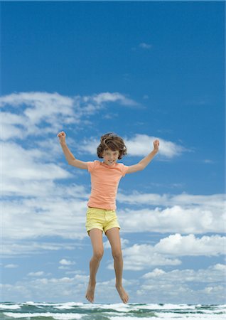 Girl jumping, sky and ocean in background, full length Stock Photo - Premium Royalty-Free, Code: 696-03401199