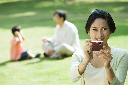 simsearch:696-03401224,k - Woman aiming digital camera, smiling at camera Stock Photo - Premium Royalty-Free, Code: 696-03401223