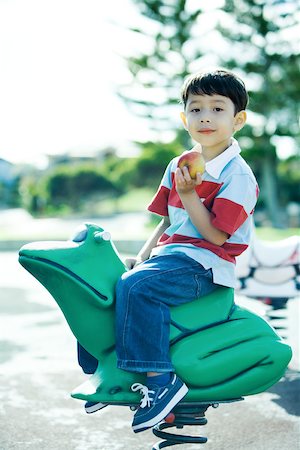 Boy on playground equipment, smiling at camera, holding apple Stock Photo - Premium Royalty-Free, Code: 696-03401538