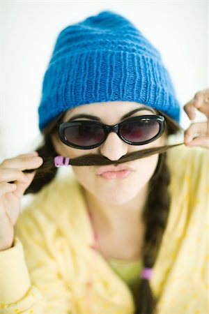 Young woman wearing knit hat and sunglasses, holding end of pigtail over upper lip, portrait Stock Photo - Premium Royalty-Free, Code: 696-03401556