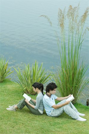 simsearch:695-03377942,k - Young adult couple reading outdoors, sitting back to back on grass by edge of lake Foto de stock - Royalty Free Premium, Número: 696-03401611