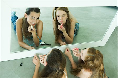 simsearch:632-01277233,k - Two friends lying on ground, applying lipstick, looking in mirror, one looking at camera Fotografie stock - Premium Royalty-Free, Codice: 696-03401711