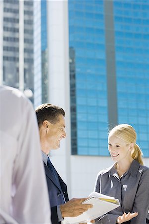 simsearch:632-01155400,k - Business associates talking about file outdoors, smiling, office building in background Stock Photo - Premium Royalty-Free, Code: 696-03401731