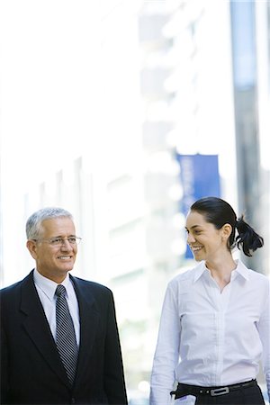 simsearch:632-01155400,k - Mature businessman and young businesswoman side by side on city sidewalk, woman looking at man Stock Photo - Premium Royalty-Free, Code: 696-03401732