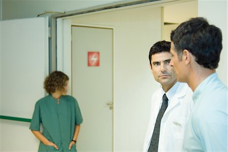 patients and doctors looking at camera hallway - Man standing with doctor in hospital, side view, woman in background Stock Photo - Premium Royalty-Free, Code: 696-03401784