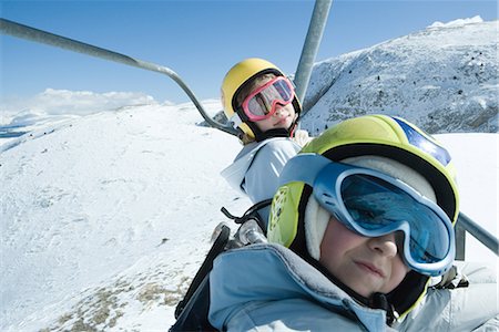 Deux jeunes amis sur remontées mécaniques, les deux portant lunettes de ski, un appareil photo en regardant Photographie de stock - Premium Libres de Droits, Code: 696-03401823