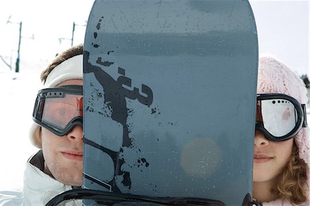 smile snowboard - Two young friends peeking at camera from behind snowboard, portrait Stock Photo - Premium Royalty-Free, Code: 696-03401926