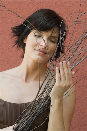 simsearch:696-03401960,k - Brunette woman holding bundle of bare branches, red wall in background, head and shoulders Stock Photo - Premium Royalty-Free, Code: 696-03401957