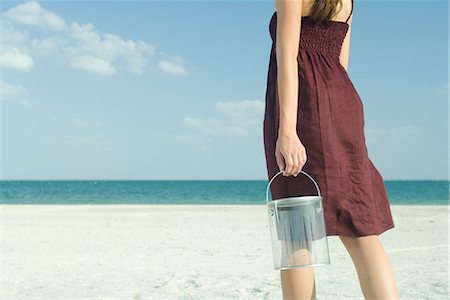 Woman standing on beach, holding bucket, cropped, rear view Stock Photo - Premium Royalty-Free, Code: 696-03401952