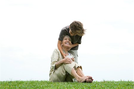 surprised grandmother - Senior woman sitting on grass, grandson standing behind her with hand on her face, giving her gift Stock Photo - Premium Royalty-Free, Code: 696-03401990