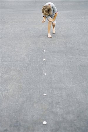 reversal - Boy placing trail of pebbles on asphalt Stock Photo - Premium Royalty-Free, Code: 696-03402024