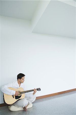 Young man sitting on floor, playing guitar, full length Stock Photo - Premium Royalty-Free, Code: 696-03402028