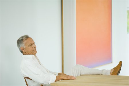 Mature man sitting at table with leg up, eyes closed Stock Photo - Premium Royalty-Free, Code: 696-03402063