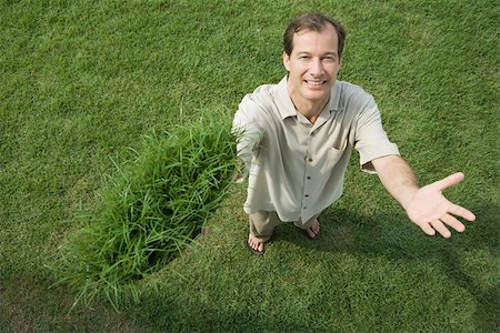 Man standing and holding clump of grass in one hand, smiling at camera, high angle view Stock Photo - Premium Royalty-Free, Code: 696-03402071