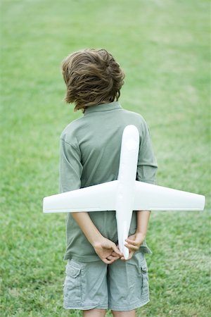 Boy holding toy airplane behind back, rear view Stock Photo - Premium Royalty-Free, Code: 696-03402137