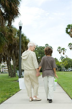 sidewalk palm trees pictures - Boy and grandmother walking on sidewalk, carrying shopping bags, talking, rear view Stock Photo - Premium Royalty-Free, Code: 696-03402153