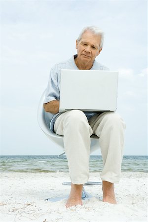 Senior man sitting in chair on beach, using laptop Stock Photo - Premium Royalty-Free, Code: 696-03402164