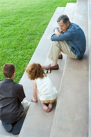 Grandfather and two grandchildren playing with toy cars together on stairs, high angle view Stock Photo - Premium Royalty-Free, Code: 696-03402179