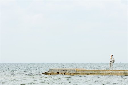 Man standing on pier, looking up, in the distance Stock Photo - Premium Royalty-Free, Code: 696-03402187