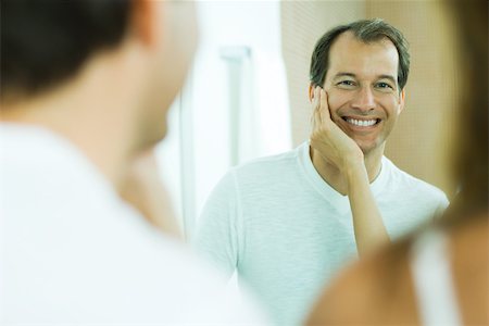 Man with wife's hand on his cheek, smiling at reflection in mirror, over the shoulder view Stock Photo - Premium Royalty-Free, Code: 696-03402228