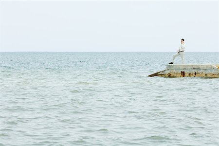 Man standing at the end of pier, talking on cell phone, in the distance Stock Photo - Premium Royalty-Free, Code: 696-03402268