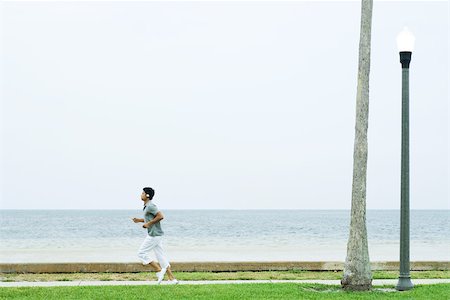 Man running at the beach, listening to headphones, side view Stock Photo - Premium Royalty-Free, Code: 696-03402269