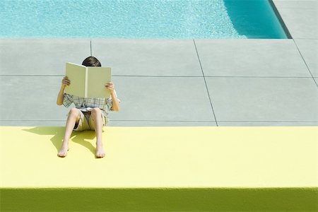 Boy reading beside swimming pool, face obscured by book, high angle view Foto de stock - Sin royalties Premium, Código: 696-03402276