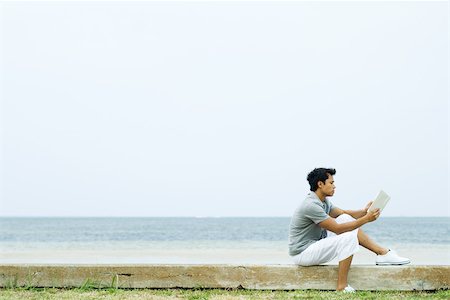 simsearch:695-03377942,k - Man sitting on low wall at the beach, reading book,  side view Stock Photo - Premium Royalty-Free, Code: 696-03402273