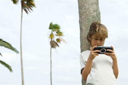 simsearch:6108-07969509,k - Boy leaning against tree trunk, playing handheld video game Stock Photo - Premium Royalty-Free, Code: 696-03402283