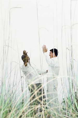 simsearch:695-03373539,k - Two men greeting each other outdoors, hands raised, viewed through tall grass Stock Photo - Premium Royalty-Free, Code: 696-03402314
