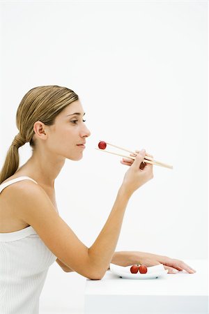simsearch:633-01992708,k - Young woman sitting, eating grape with chopsticks, side view Stock Photo - Premium Royalty-Free, Code: 696-03402376