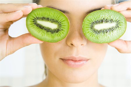 Woman holding kiwi halves in front of her eyes, smiling, headshot Stock Photo - Premium Royalty-Free, Code: 696-03402528