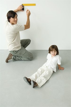 parent child measure - Man measuring wall with a ruler, son sitting nearby, both smiling at camera Stock Photo - Premium Royalty-Free, Code: 696-03402628