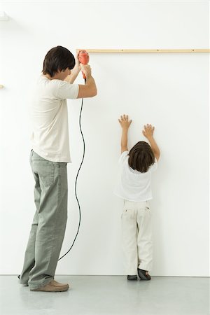 Perçage du mur, son fils pouvant atteindre, en essayant d'aider l'homme Photographie de stock - Premium Libres de Droits, Code: 696-03402630