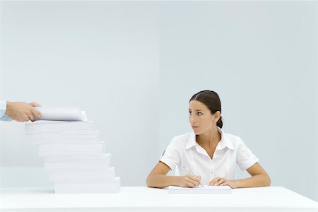 Femme assise à table, en regardant une pile échelonnée de papier, les mains de l'homme l'ajout de papier à la pile Photographie de stock - Premium Libres de Droits, Code: 696-03402651