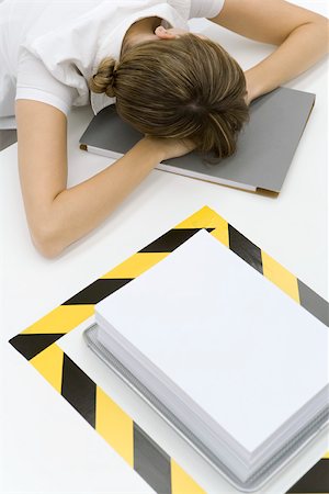 Woman sitting with her head down near a stack of paper surrounded by black and yellow tape Stock Photo - Premium Royalty-Free, Code: 696-03402665