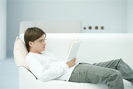 simsearch:632-03027019,k - Young man reclining on sofa, reading book, side view Stock Photo - Premium Royalty-Free, Code: 696-03402712