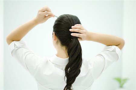 fixing hair - Woman putting hair in ponytail, arms raised, rear view Stock Photo - Premium Royalty-Free, Code: 696-03402720