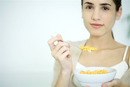 eat with cereal bowl with spoon - Young woman holding bowl of cereal, smiling at camera Stock Photo - Premium Royalty-Free, Code: 696-03402732