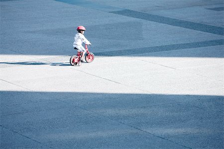 rodinha da bicicleta - Child riding bicycle alone in public square Foto de stock - Royalty Free Premium, Número: 696-03402962