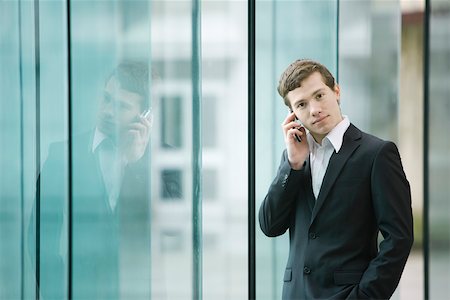 Businessman standing by glass wall talking on cell phone Stock Photo - Premium Royalty-Free, Code: 696-03402997