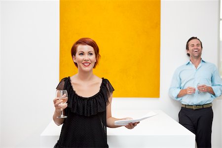 female gallery - Cheerful woman standing in front of yellow painting with man in background Stock Photo - Premium Royalty-Free, Code: 693-05552764