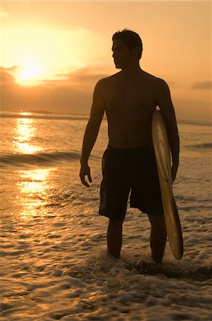 Surfer standing in surf, holding surfboard, at sunset Stock Photo - Premium Royalty-Free, Code: 693-06014635