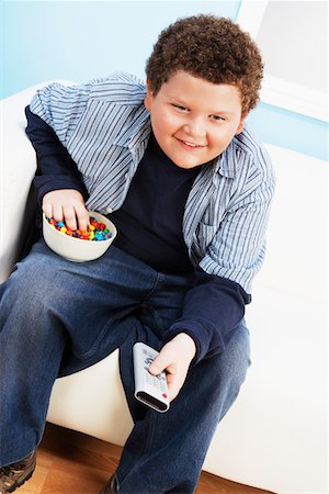 Overweight boy (13-15) Eating Junk Food, holding remote control Stock Photo - Premium Royalty-Free, Code: 693-06016255